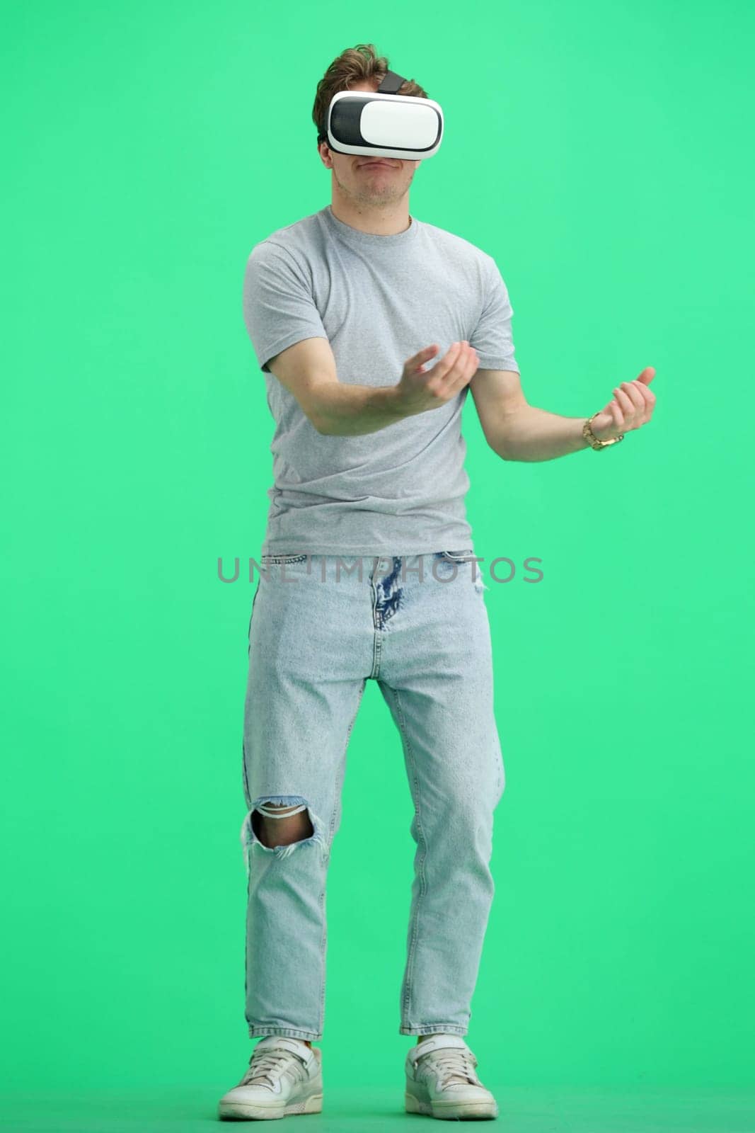 Man, full-length, on a green background, wearing VR glasses.