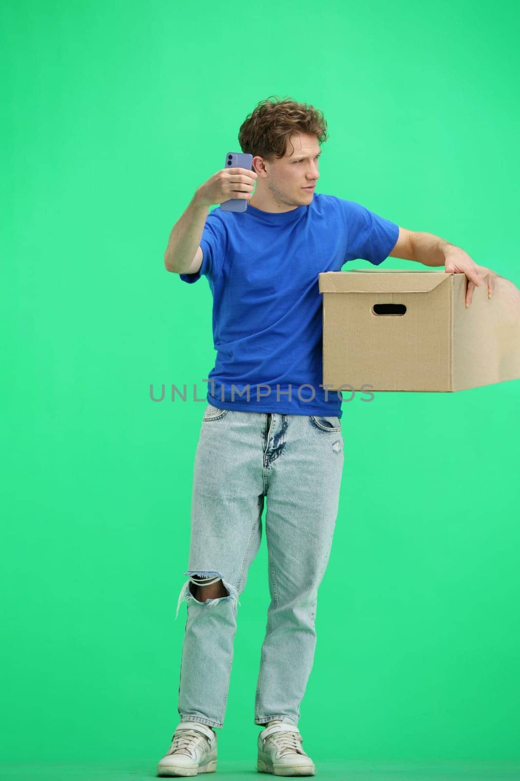The deliveryman, in full height, on a green background, with a box, talking on the phone by Prosto