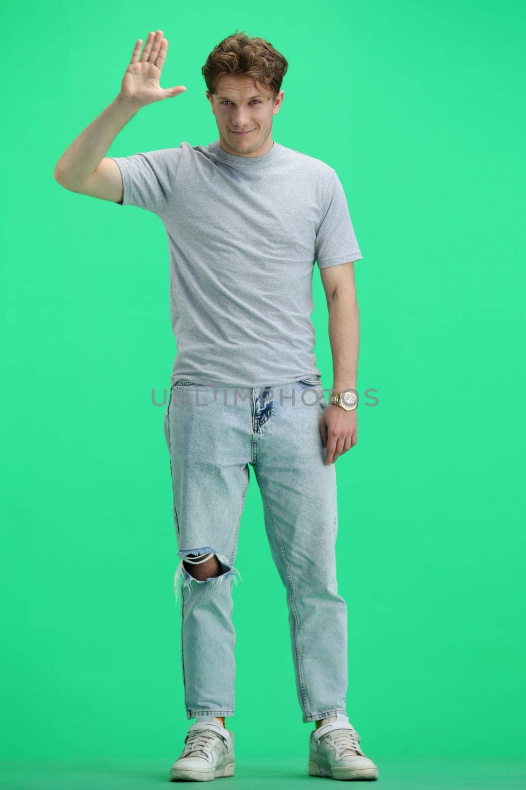 A man, full-length, on a green background, waving his hand.