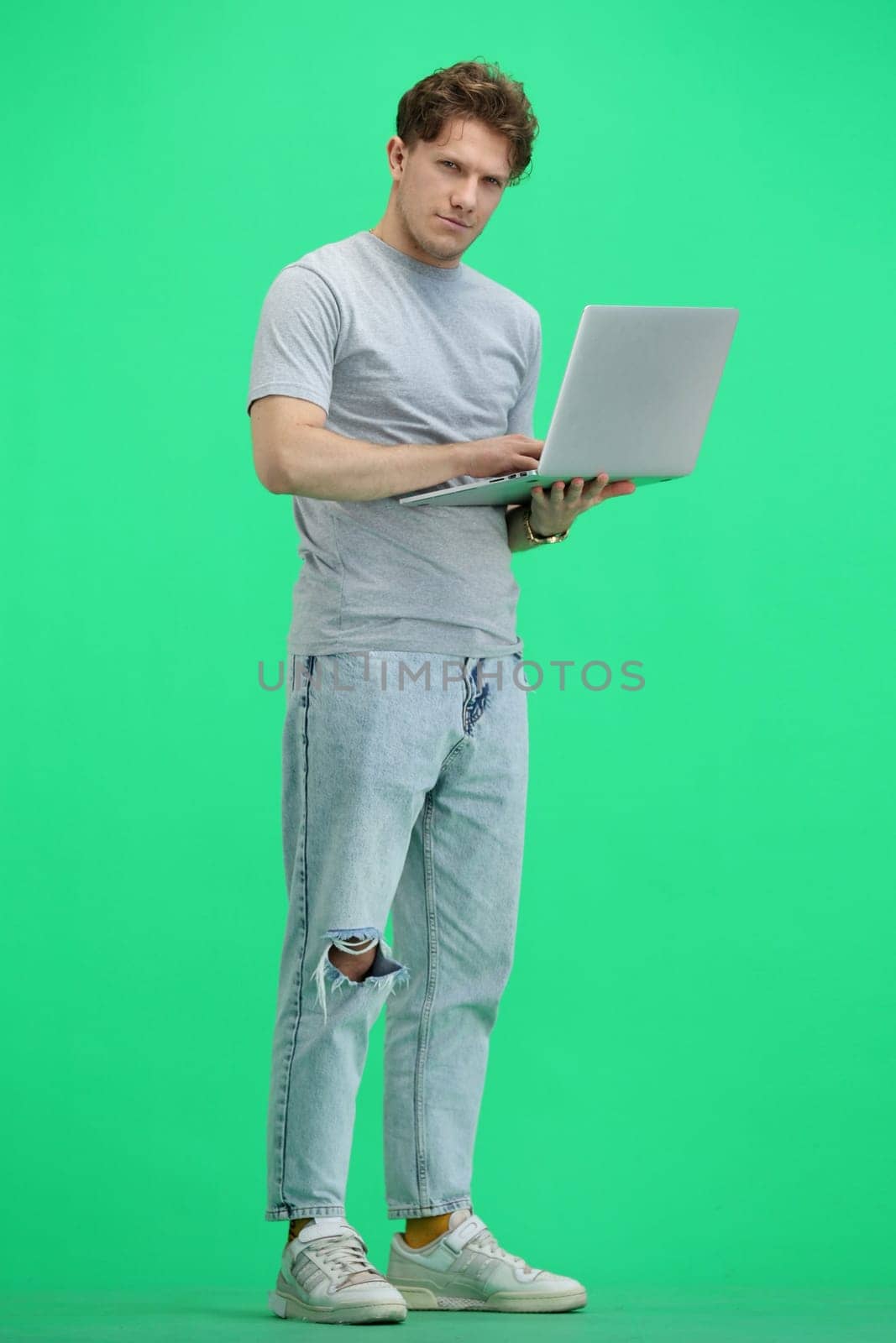 A man, full-length, on a green background, with a laptop.