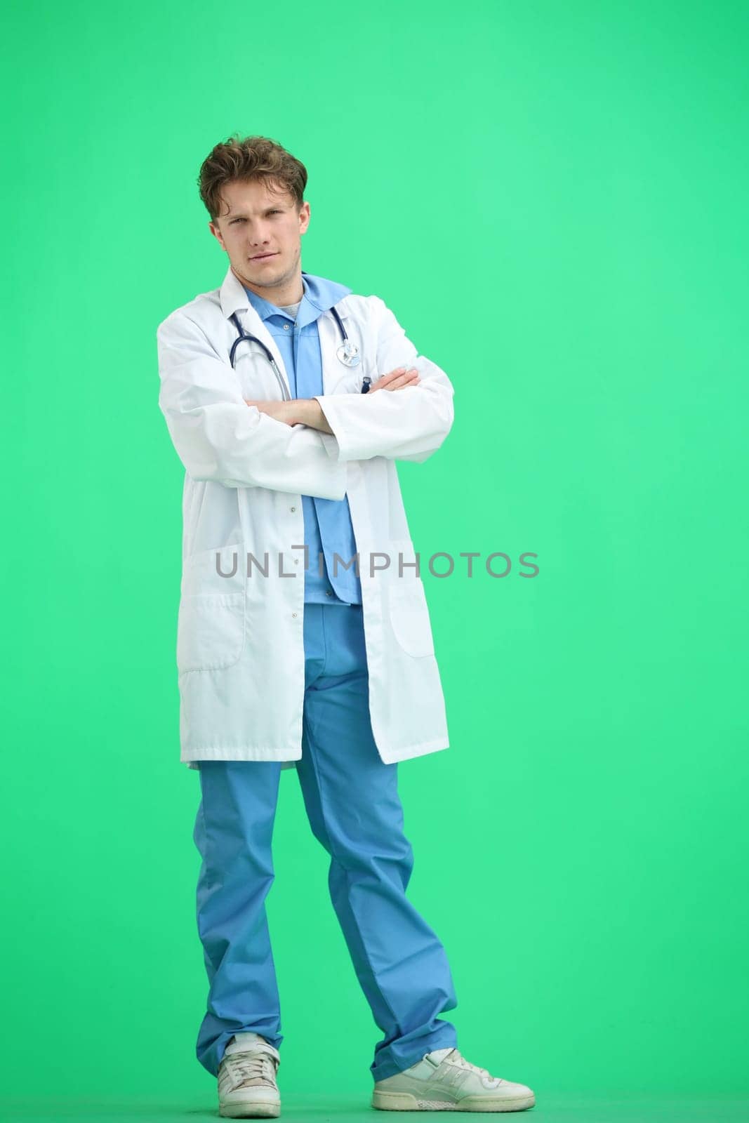 The doctor, in full height, on a green background, crossed his arms.