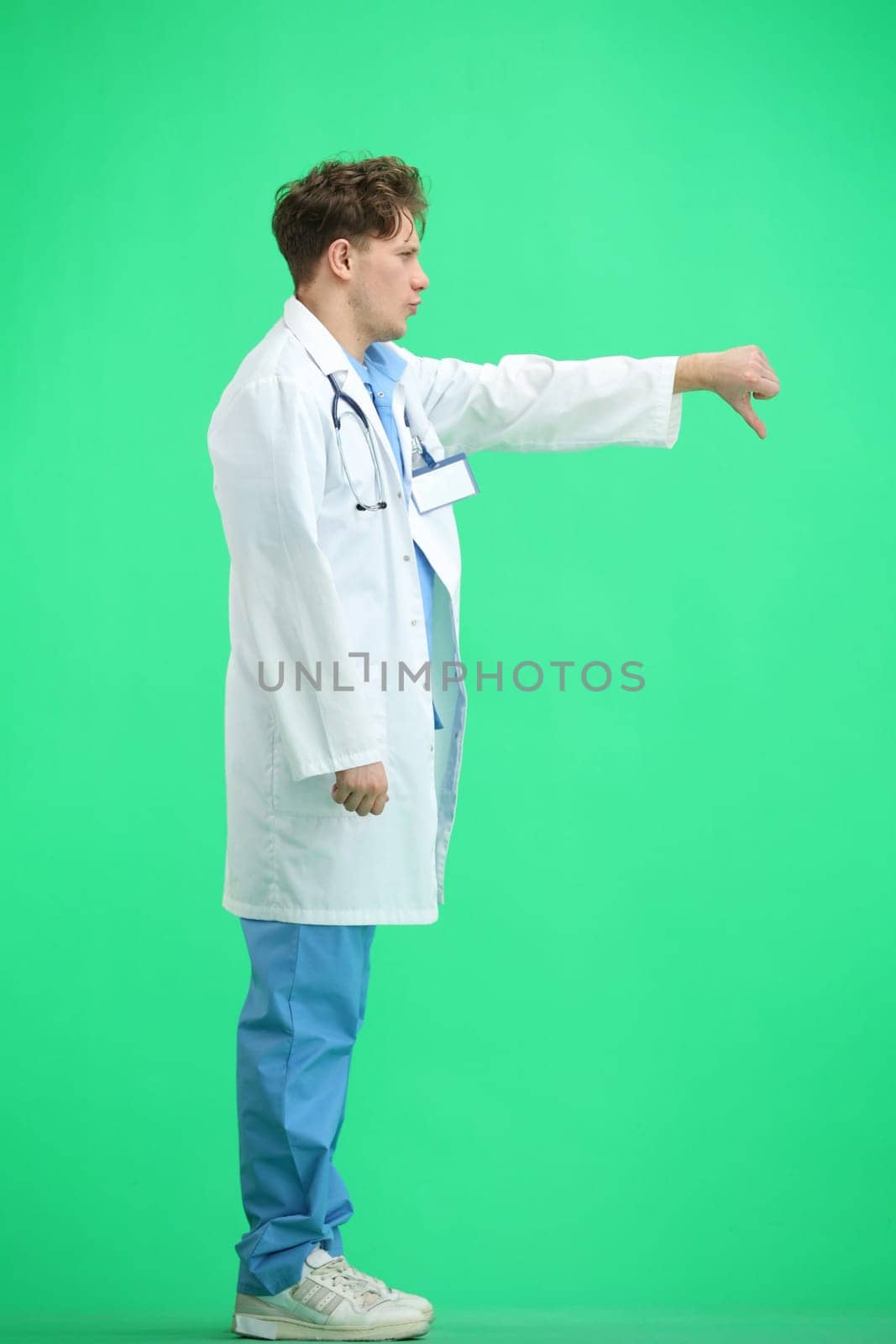 The doctor, in full height, on a green background, shows his finger down.