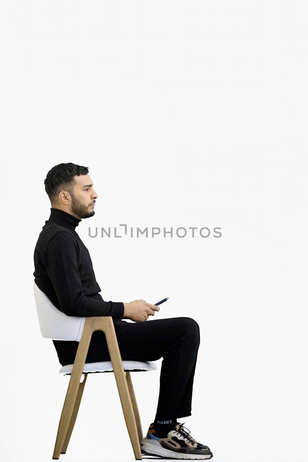 A man, full-length, on a white background, sitting on a chair.