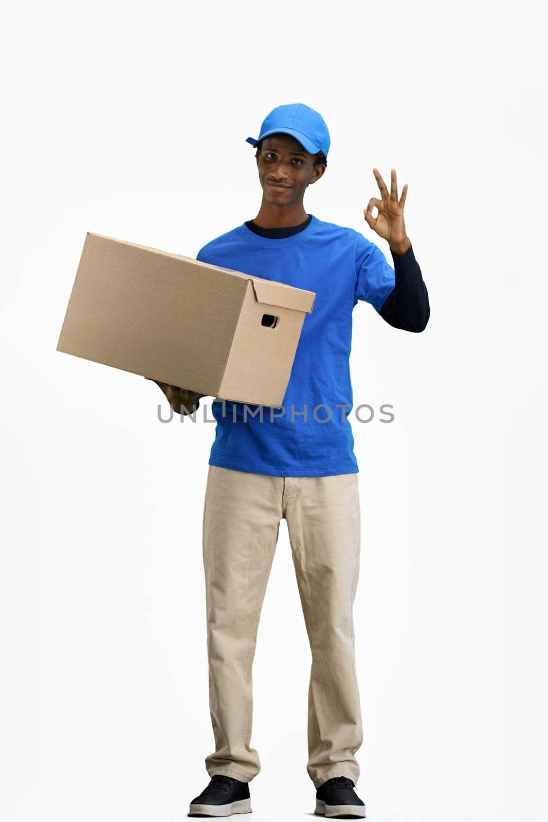The deliveryman, in full height, on a white background, with a box, shows the ok sign by Prosto