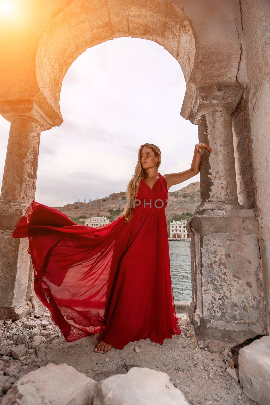 Woman red dress. Summer lifestyle of a happy woman posing near a fence with balusters over the sea. by Matiunina