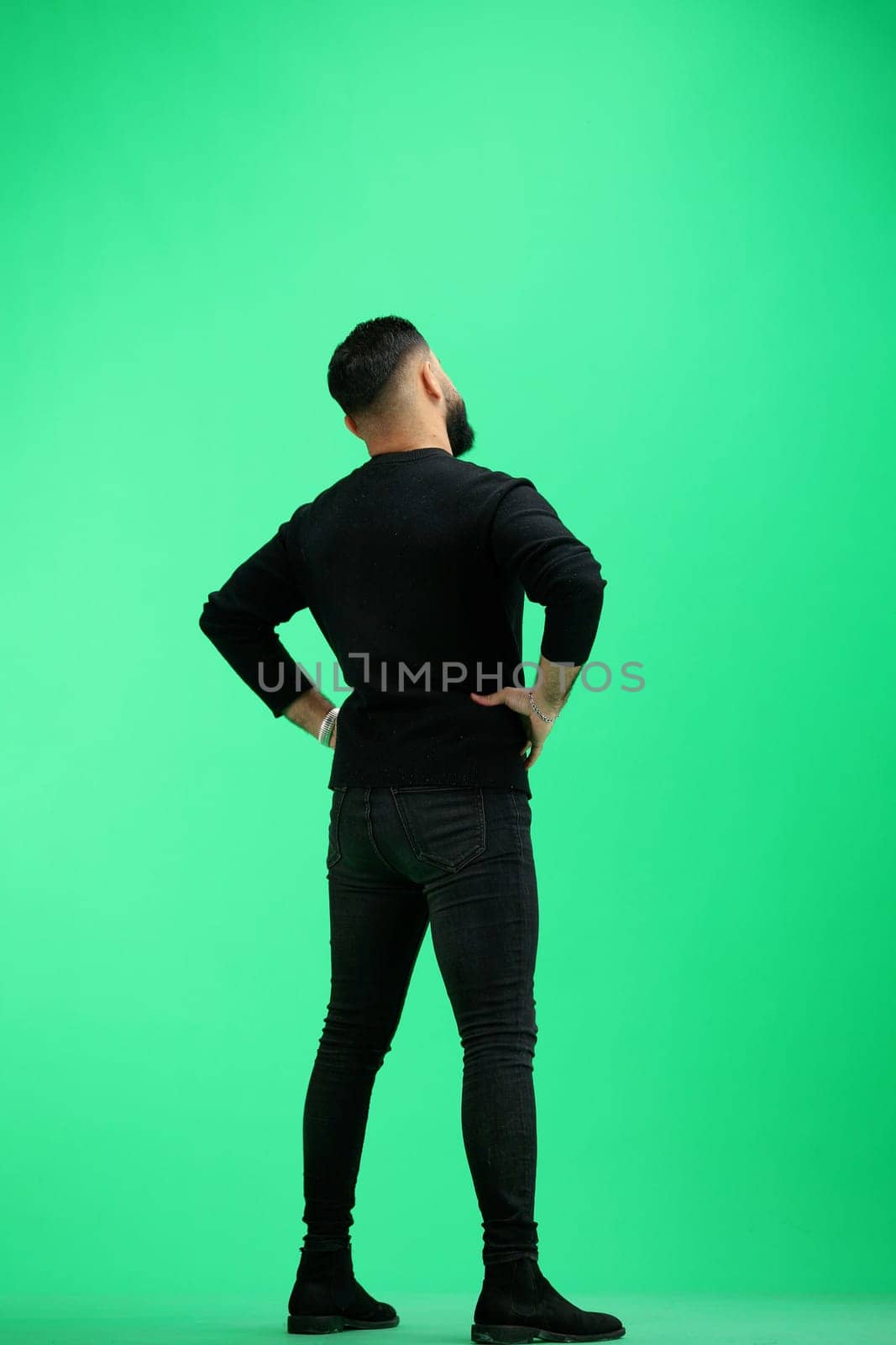 Man, full-length, on a green background, hands on hips.