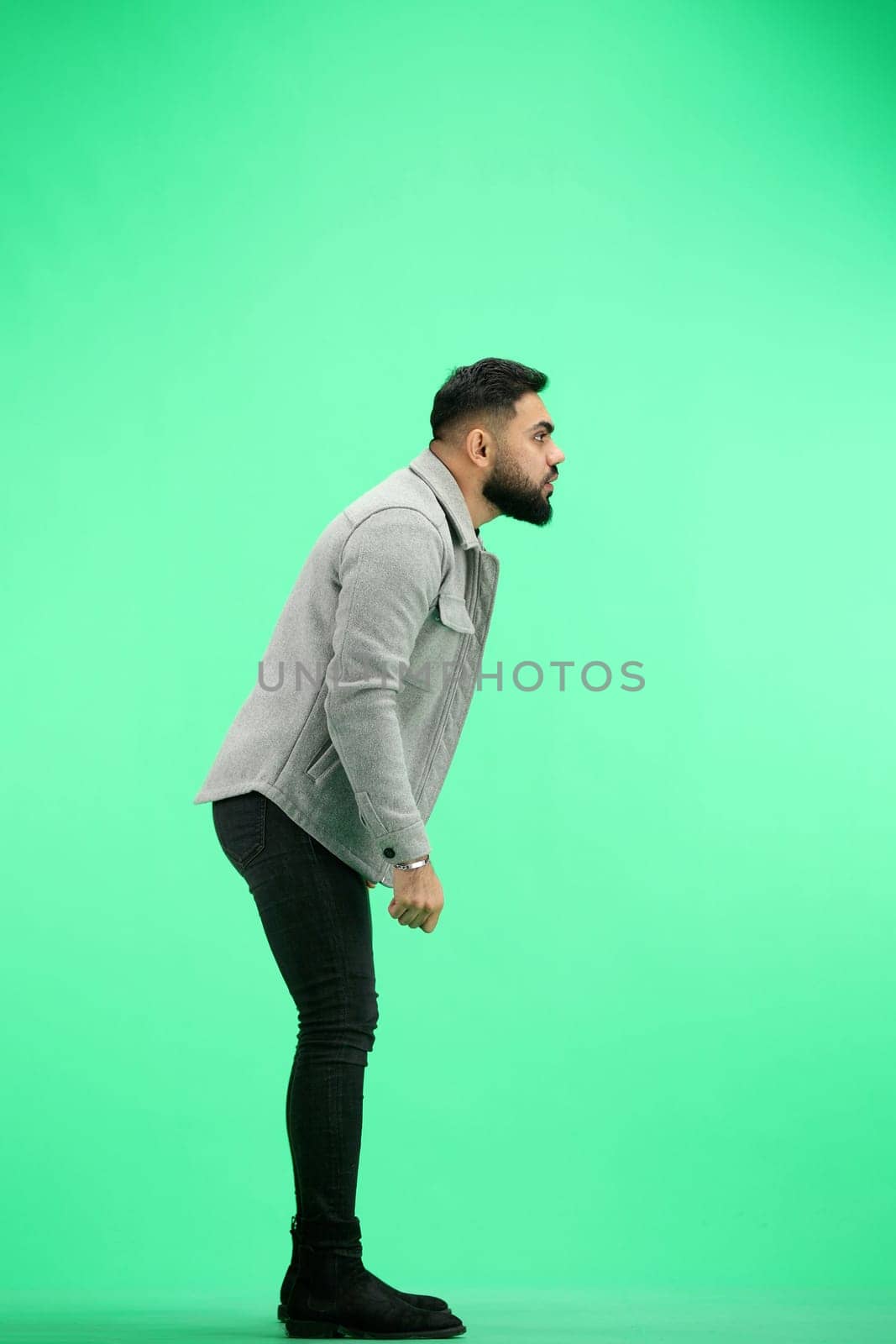 A man, full-length, on a green background, spreads his arms.