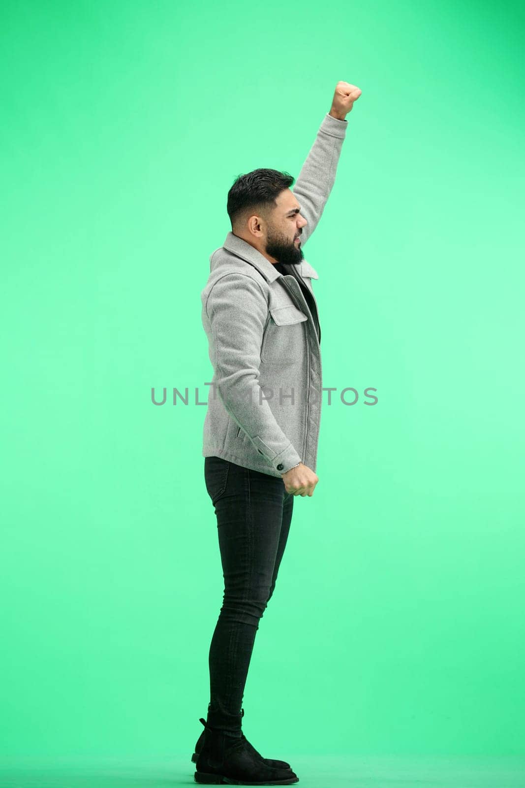 A man, full-length, on a green background, raised his hand up.