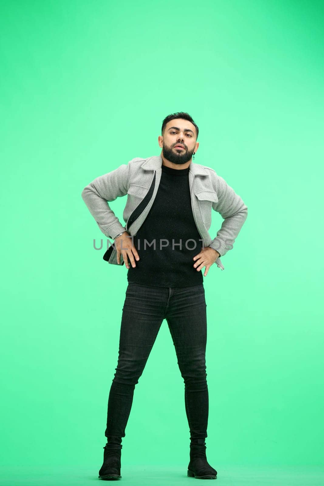 Man, full-length, on a green background, hands on hips.