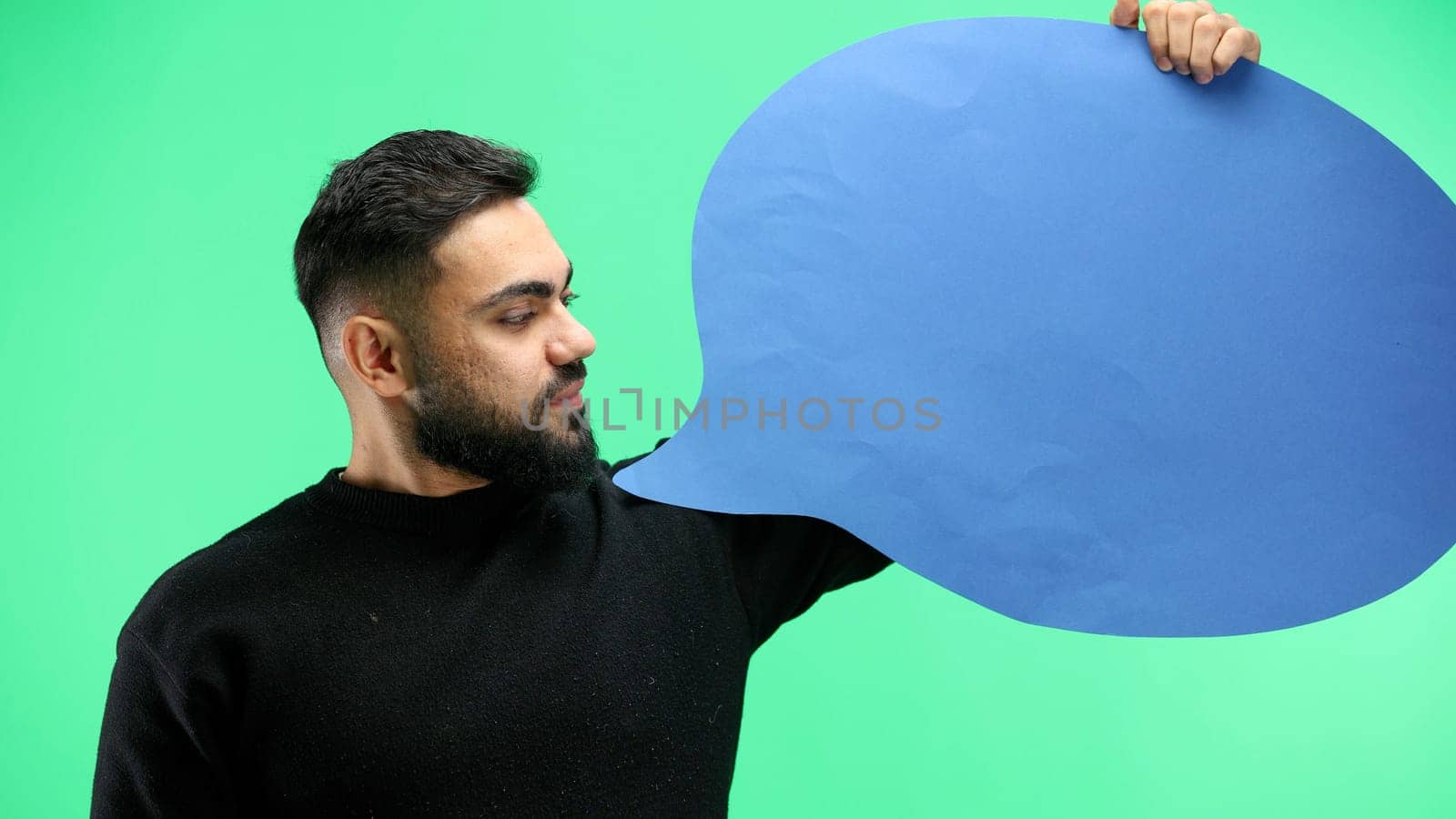A man, close-up, on a green background, shows a blue comment sign.