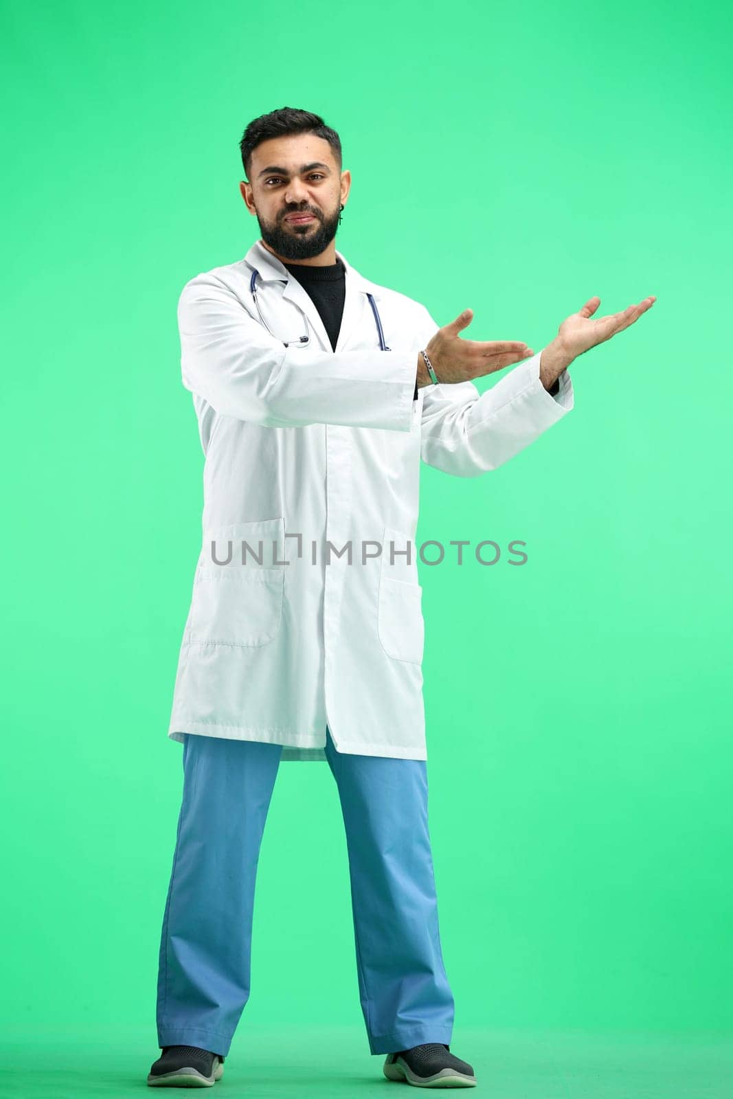 The doctor, in full height, on a green background, points to the side.