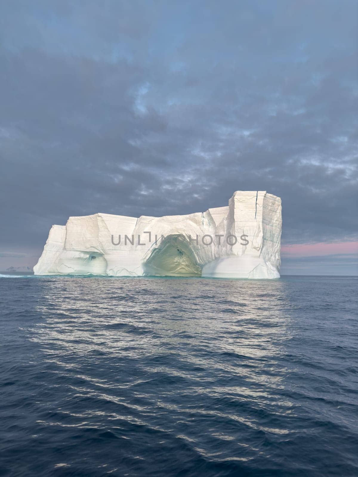 A huge high breakaway glacier drifts in the southern ocean off the coast of Antarctica at sunset, the Antarctic Peninsula, the Southern Arctic Circle, azure water, cloudy weather. High quality photo