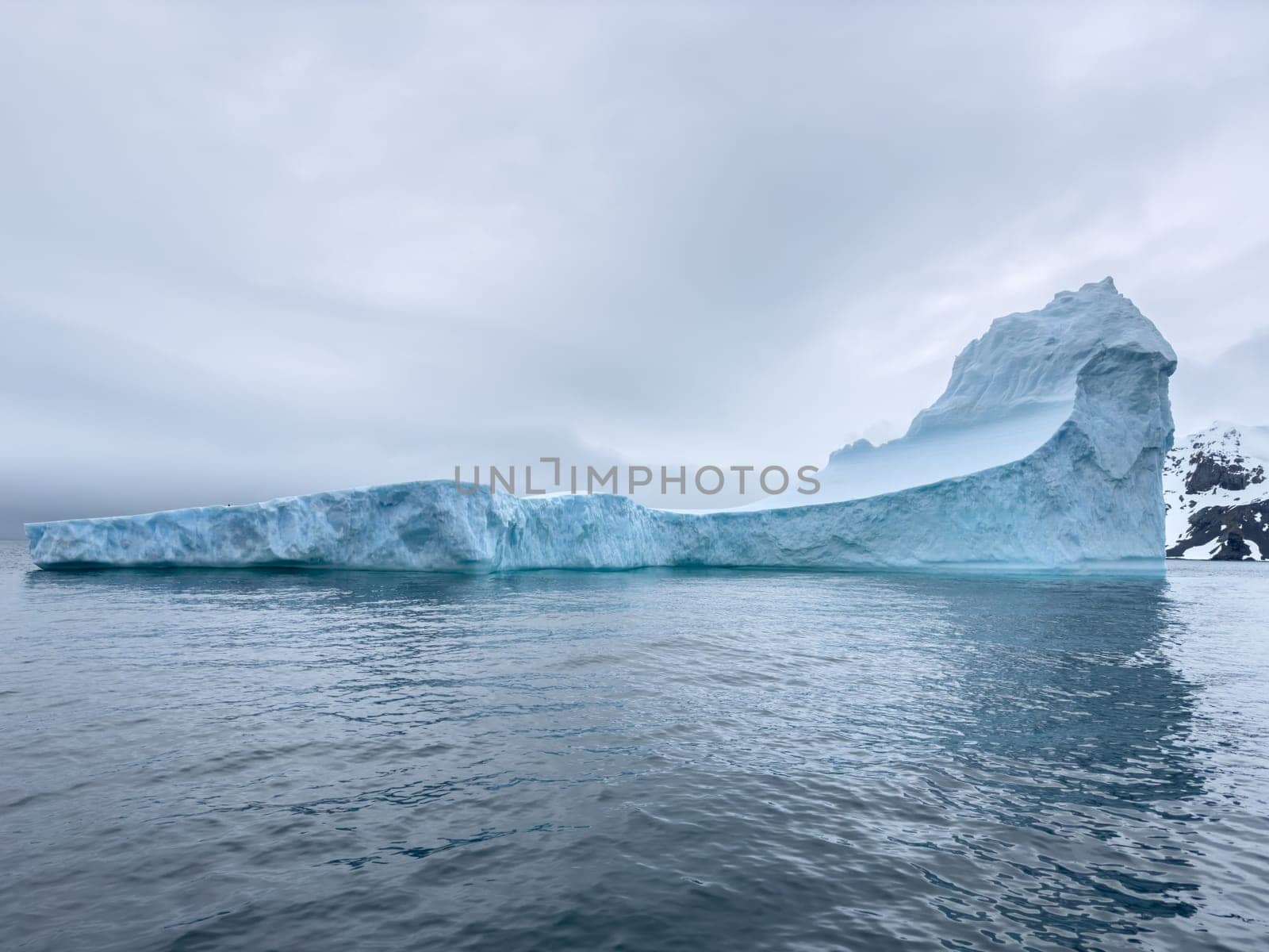 A huge high breakaway glacier drifts in the southern ocean off the coast of Antarctica at sunset, the Antarctic Peninsula, the Southern Arctic Circle, azure water, cloudy weather by vladimirdrozdin