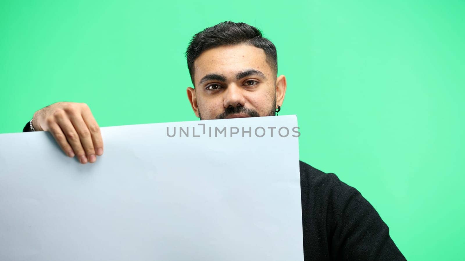 A man, close-up, on a green background, shows a white sheet.