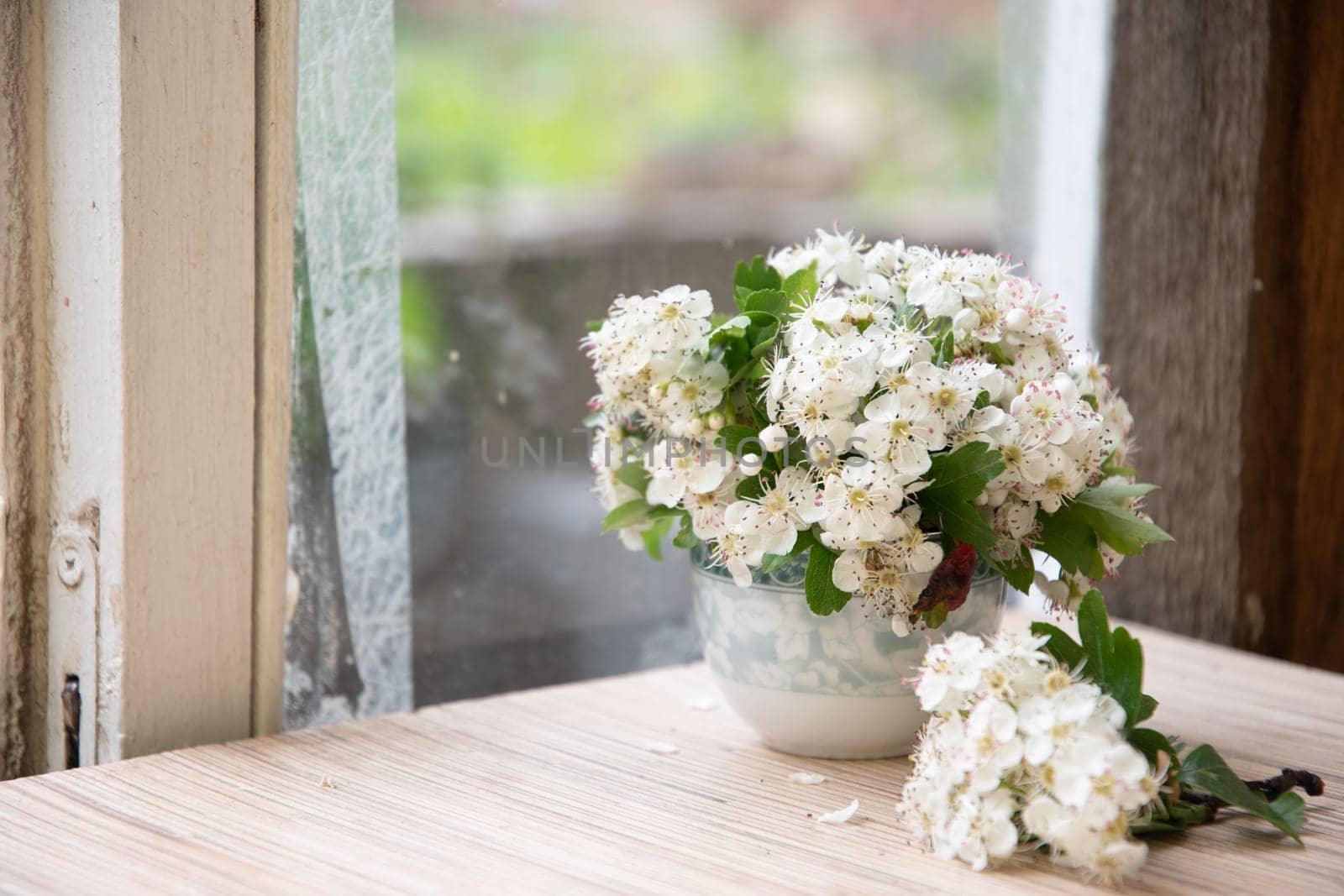 still life of small bouquet of a branch of blooming hawthorn in vase on an old dilapidated windowsill, romantic mood and spring freshness, comfort in the home, everyday decoration, high quality photo