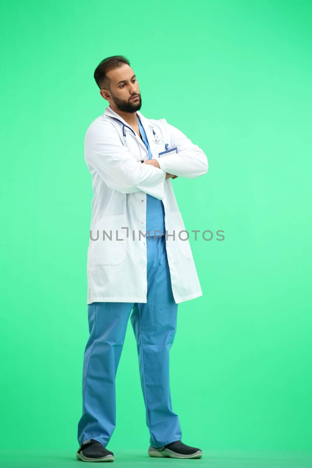 The doctor, in full height, on a green background, crossed his arms.