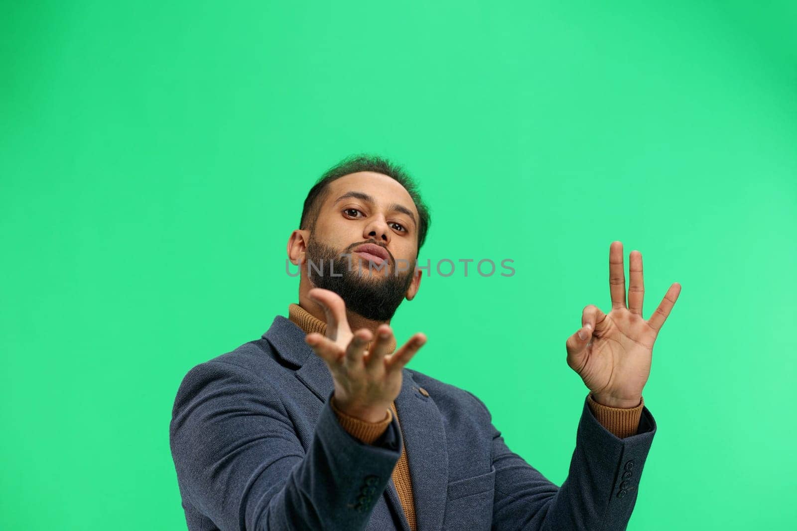A man, close-up, on a green background, shows an ok sign.