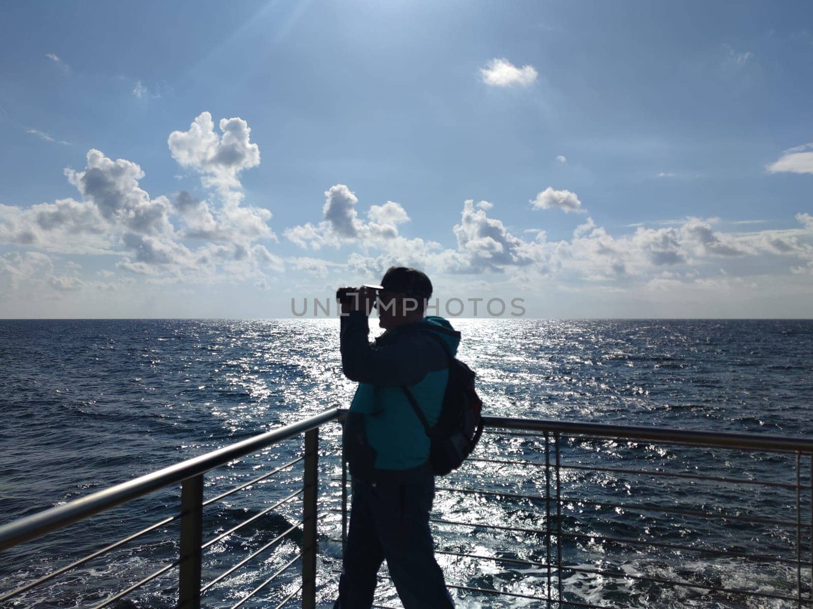 a man with a backpack looks through binoculars at the sea horizon.