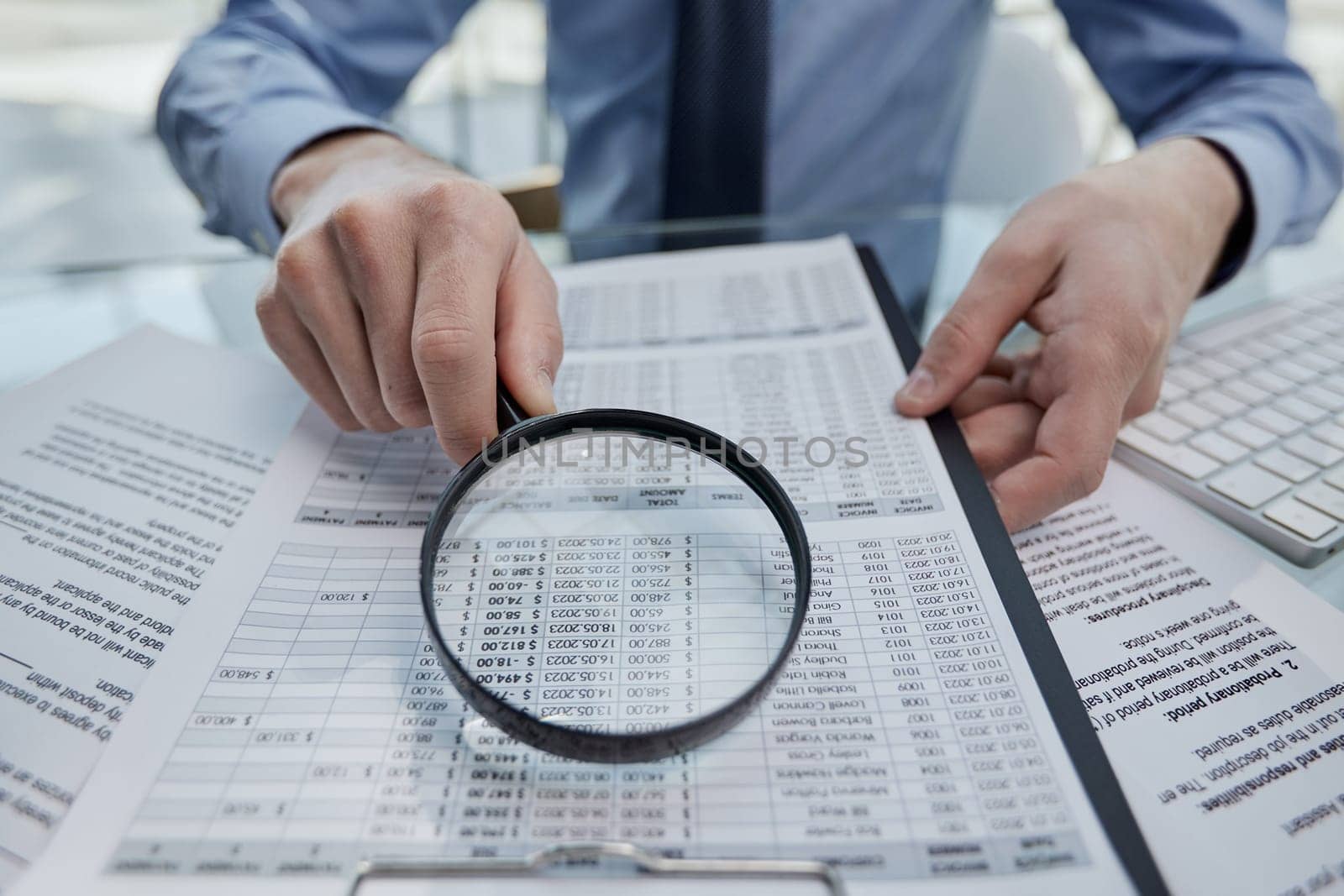 man looking through a magnifying glass to documents notebook.