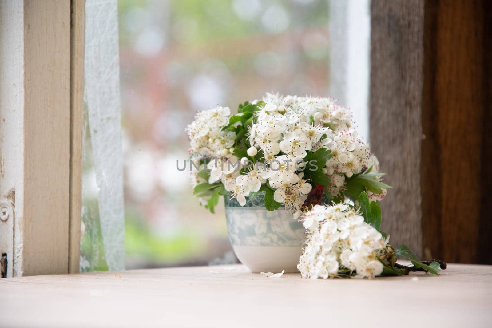still life of small bouquet of a branch of blooming hawthorn in vase on an old dilapidated windowsill, romantic mood and spring freshness, comfort in the home, everyday decoration, high quality photo
