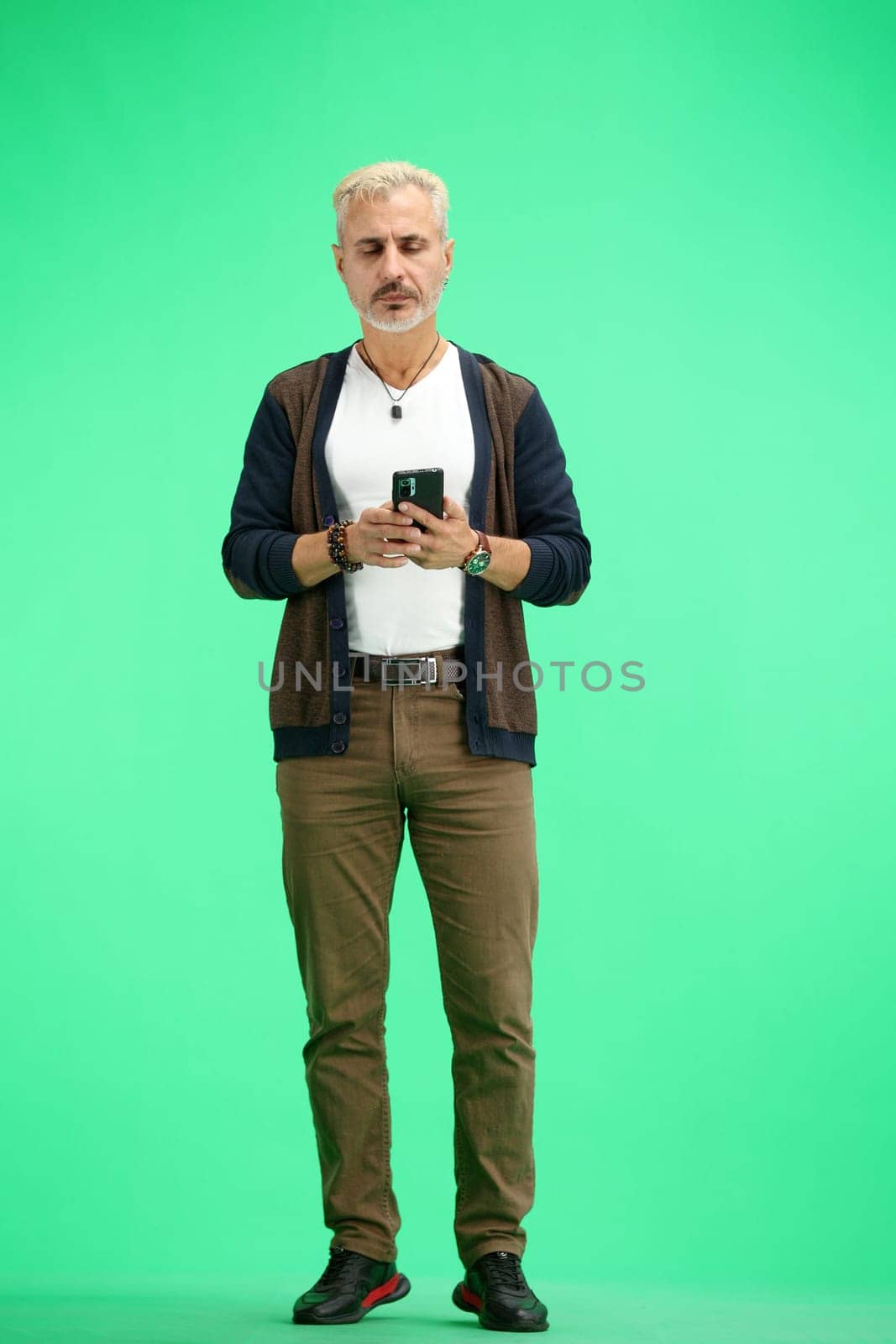 A man, full-length, on a green background, uses a phone.