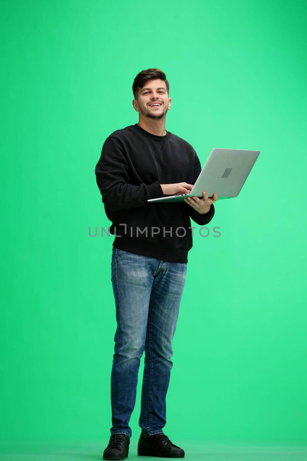 A man, full-length, on a green background, uses a phone.