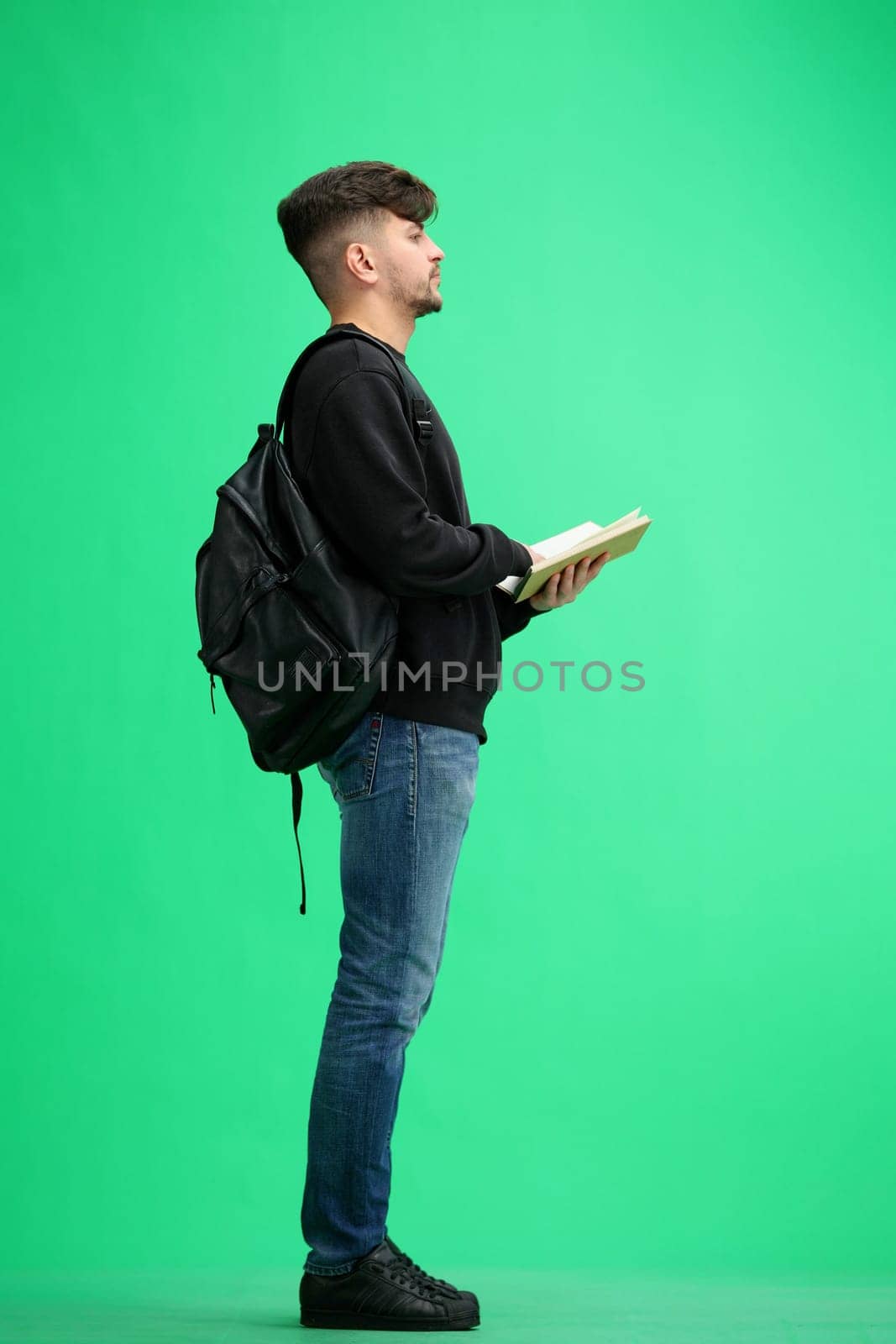 A man, full-length, on a green background, with a backpack.
