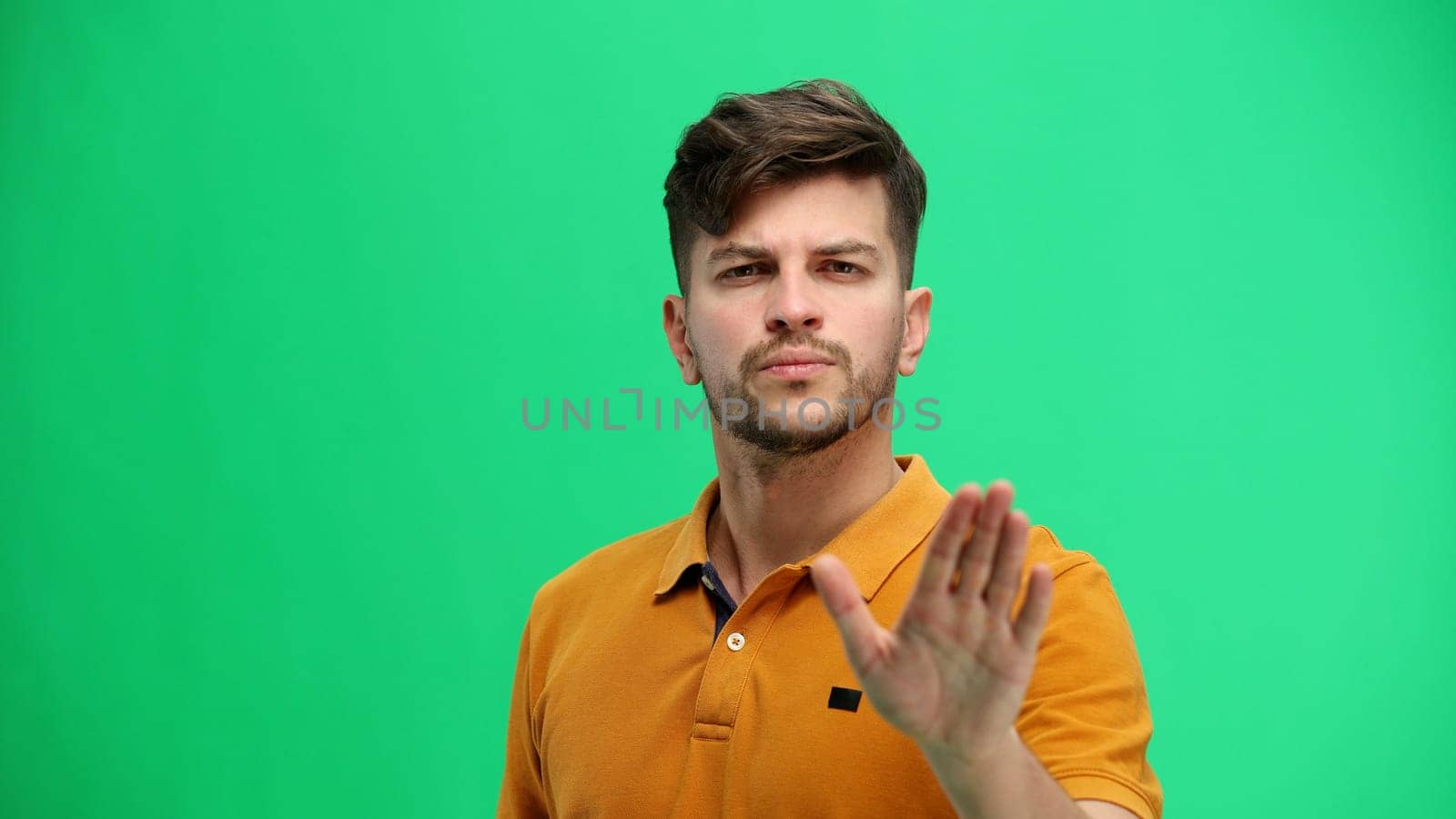 A man, close-up, on a green background, shows a stop sign.