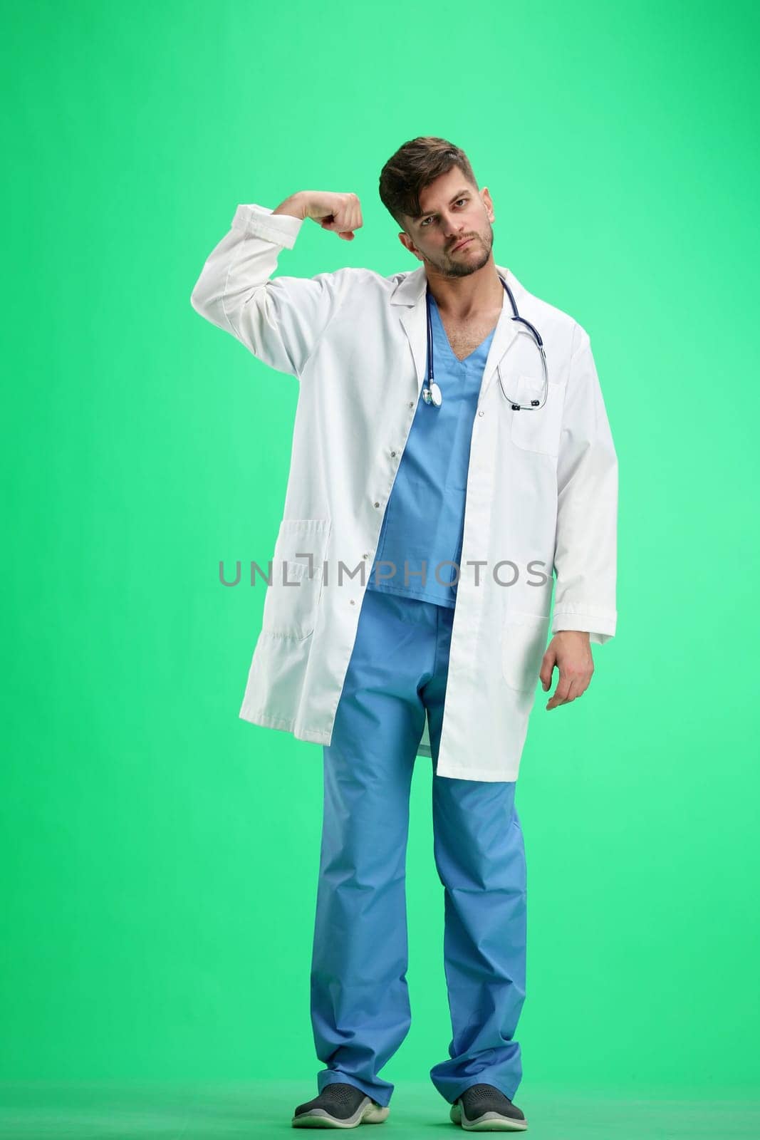 The doctor, in full height, on a green background, shows strength.
