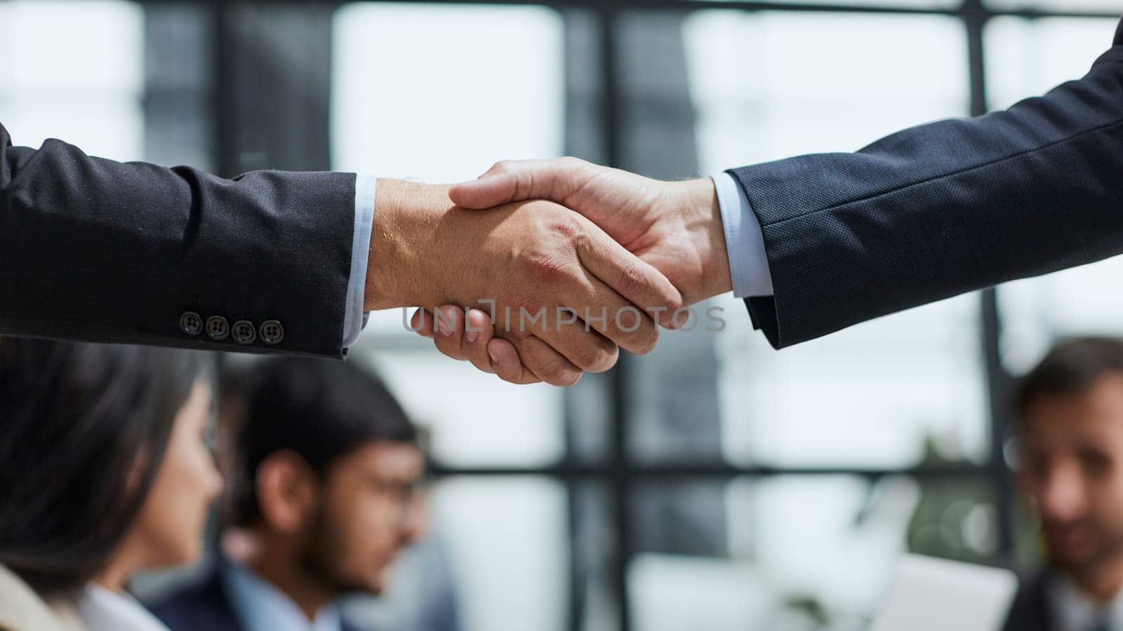 Close up view of two unrecognizable people shaking hands in office against work meeting background