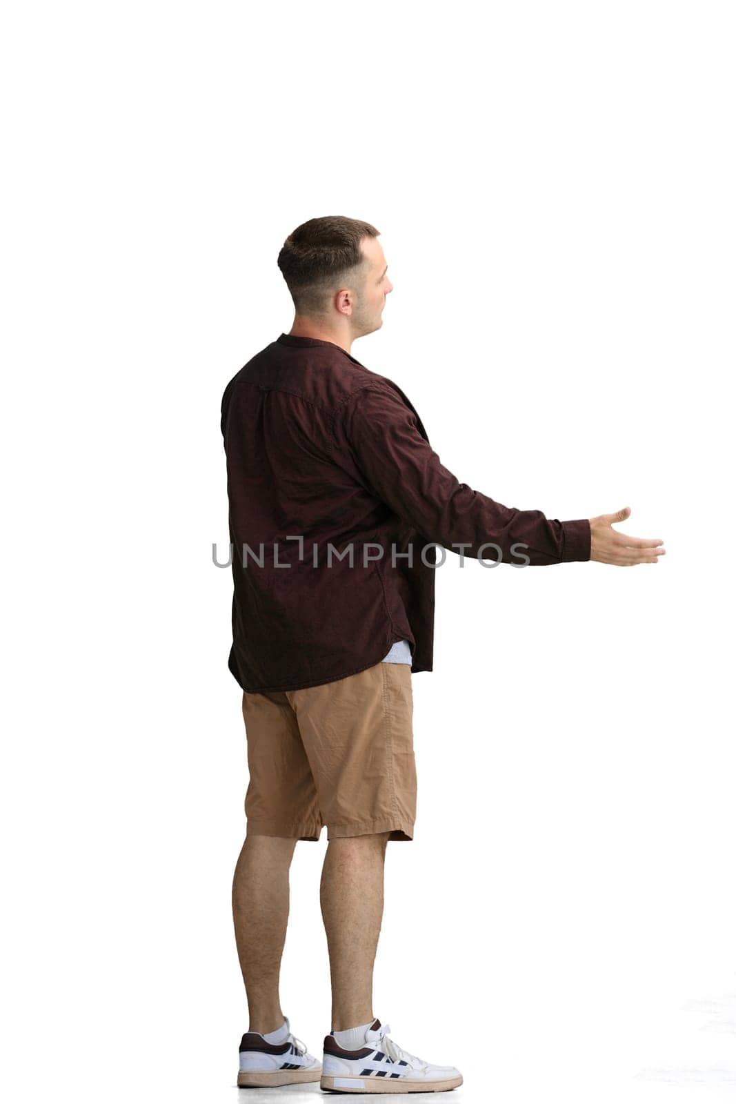 A man in a brown shirt, on a white background, in full height, looks at his watch.