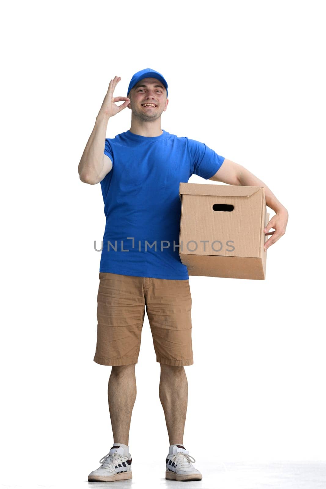 A male deliveryman, on a white background, in full height, with a box, shows the ok sign.