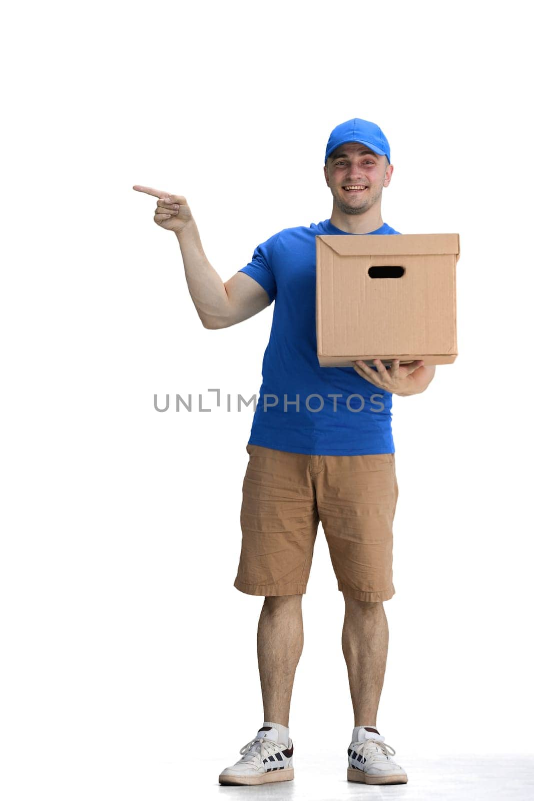 A male deliveryman, on a white background, full-length, with a box, points to the side.