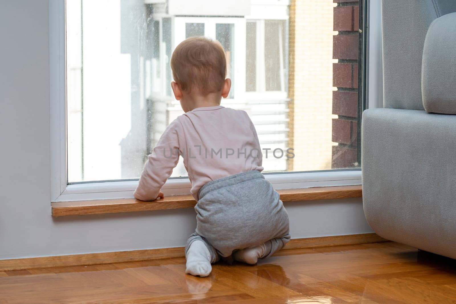 Standing at a window, a child looks out at the outside world from their apartment, wanting to explore and play. Concept of feeling trapped and dreaming of outdoor fun