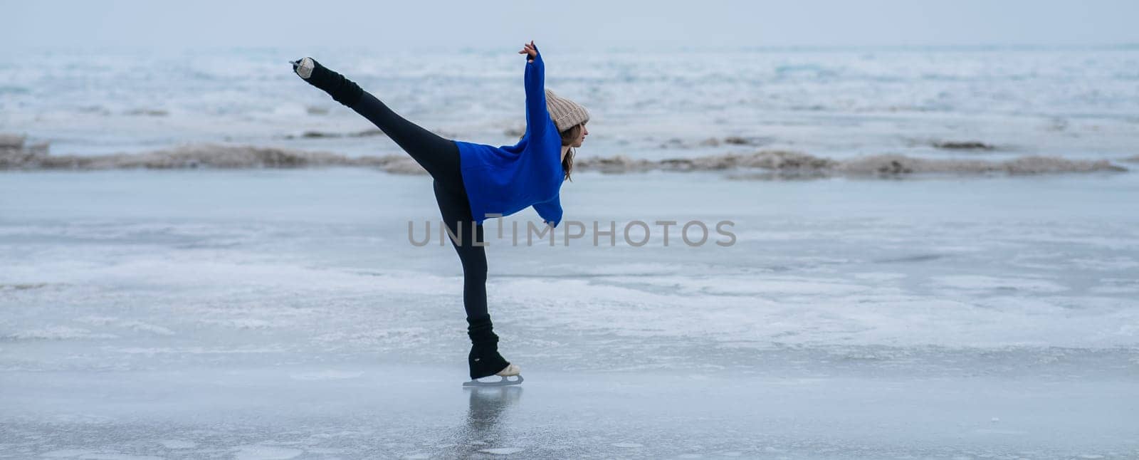 Caucasian woman in a blue sweater is skating on a frozen lake. Figure skater performs a swallow