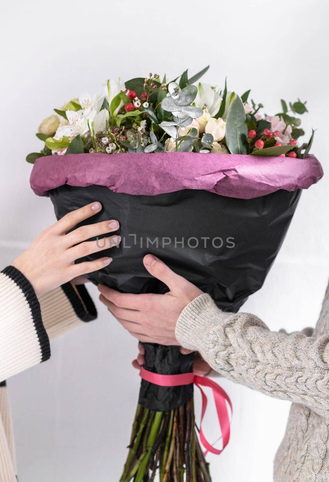 One unrecognizable Caucasian guy gives his girlfriend a large bouquet of flowers in black paper with a lilac border, close-up side view.