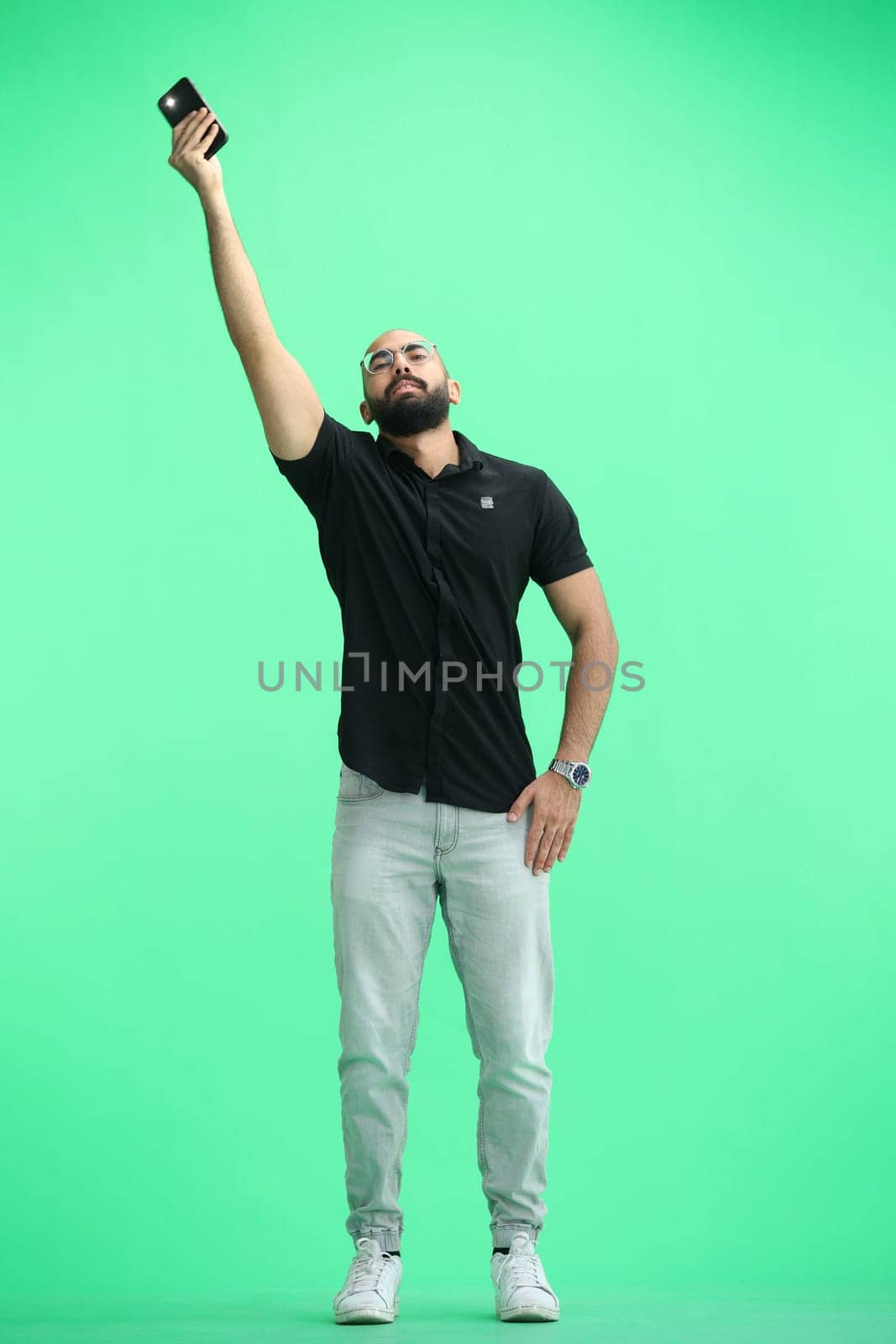 A man, on a green background, in full height, waving his phone.