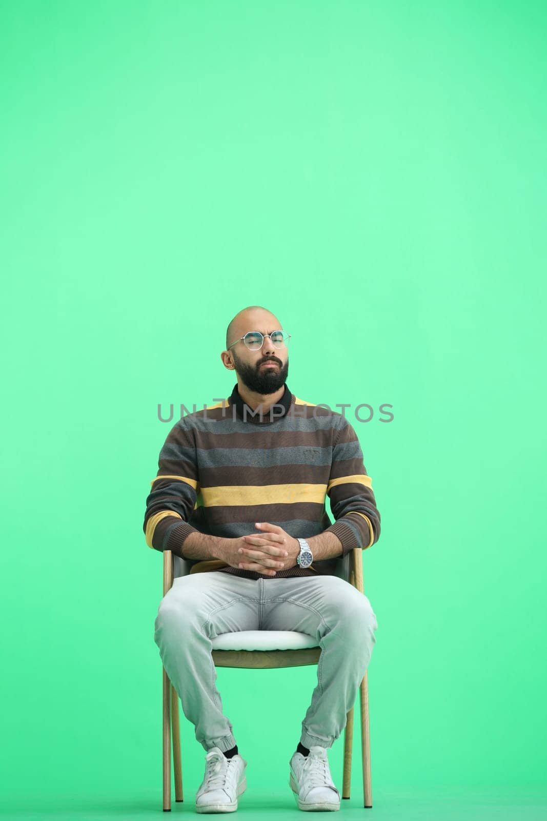 A man, on a green background, is sitting on a chair by Prosto