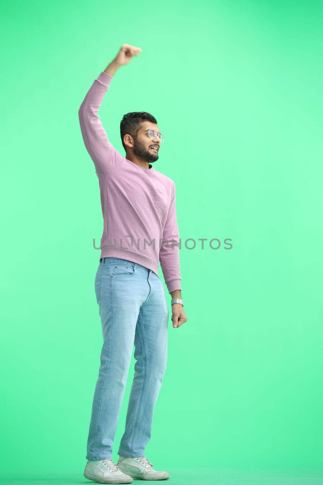 A man, on a green background, in full height, raised his hand.