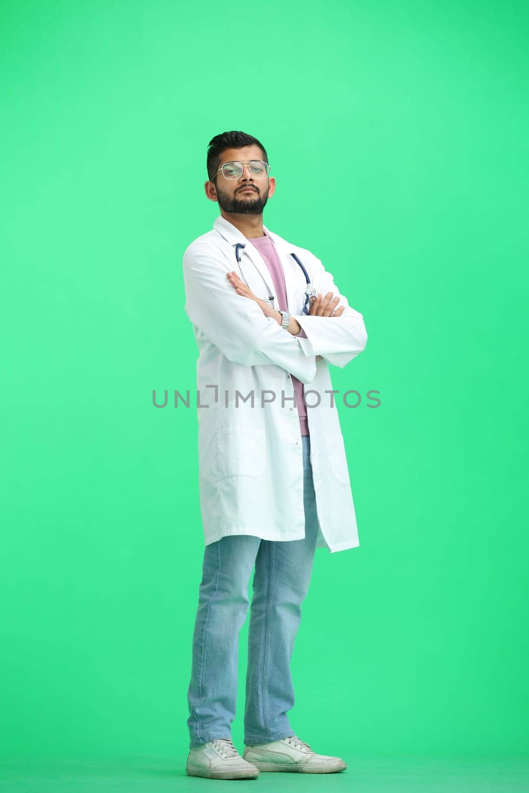 The male doctor, on a green background, in full height, crossed his arms.