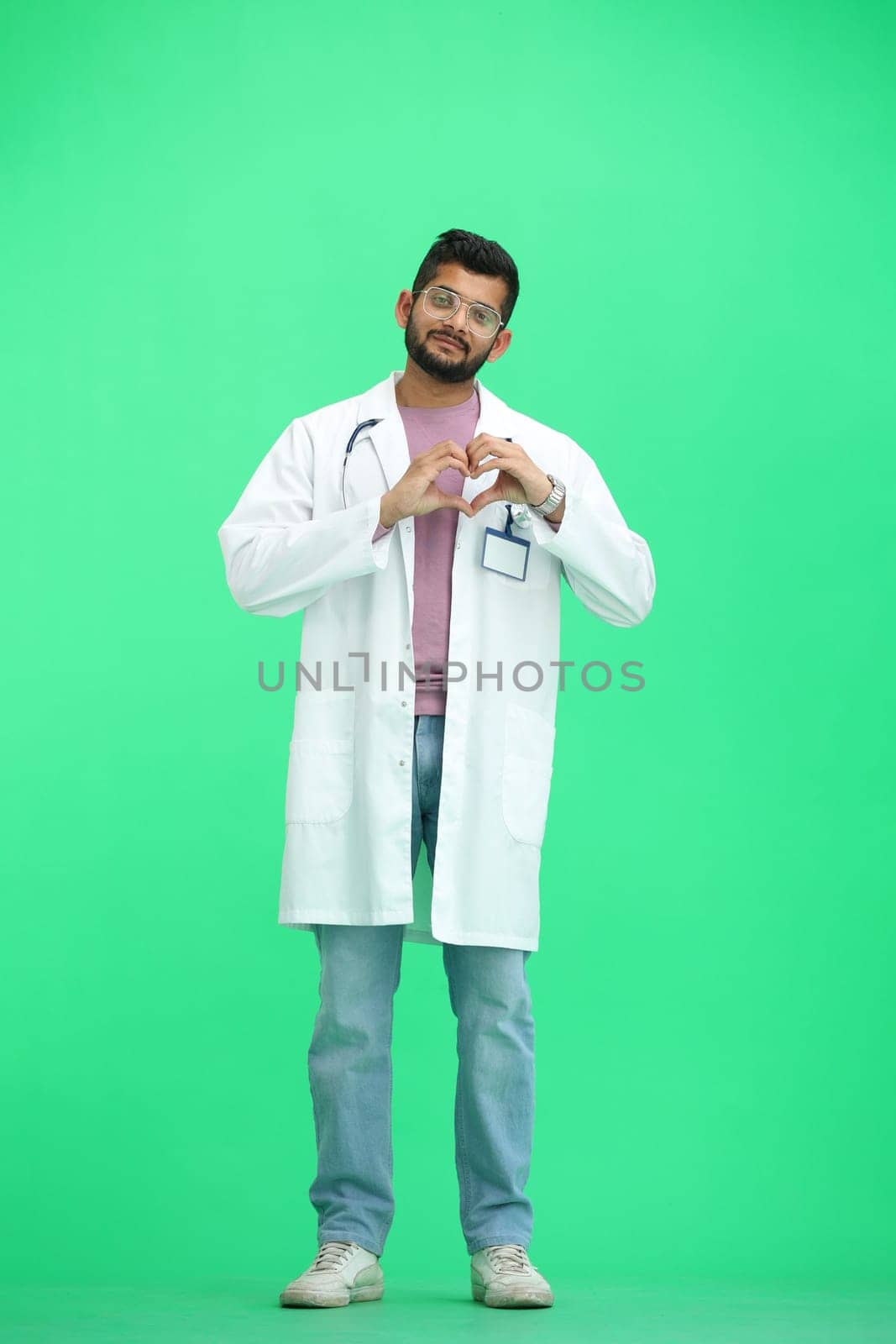 A male doctor, on a green background, in full height, shows a heart.