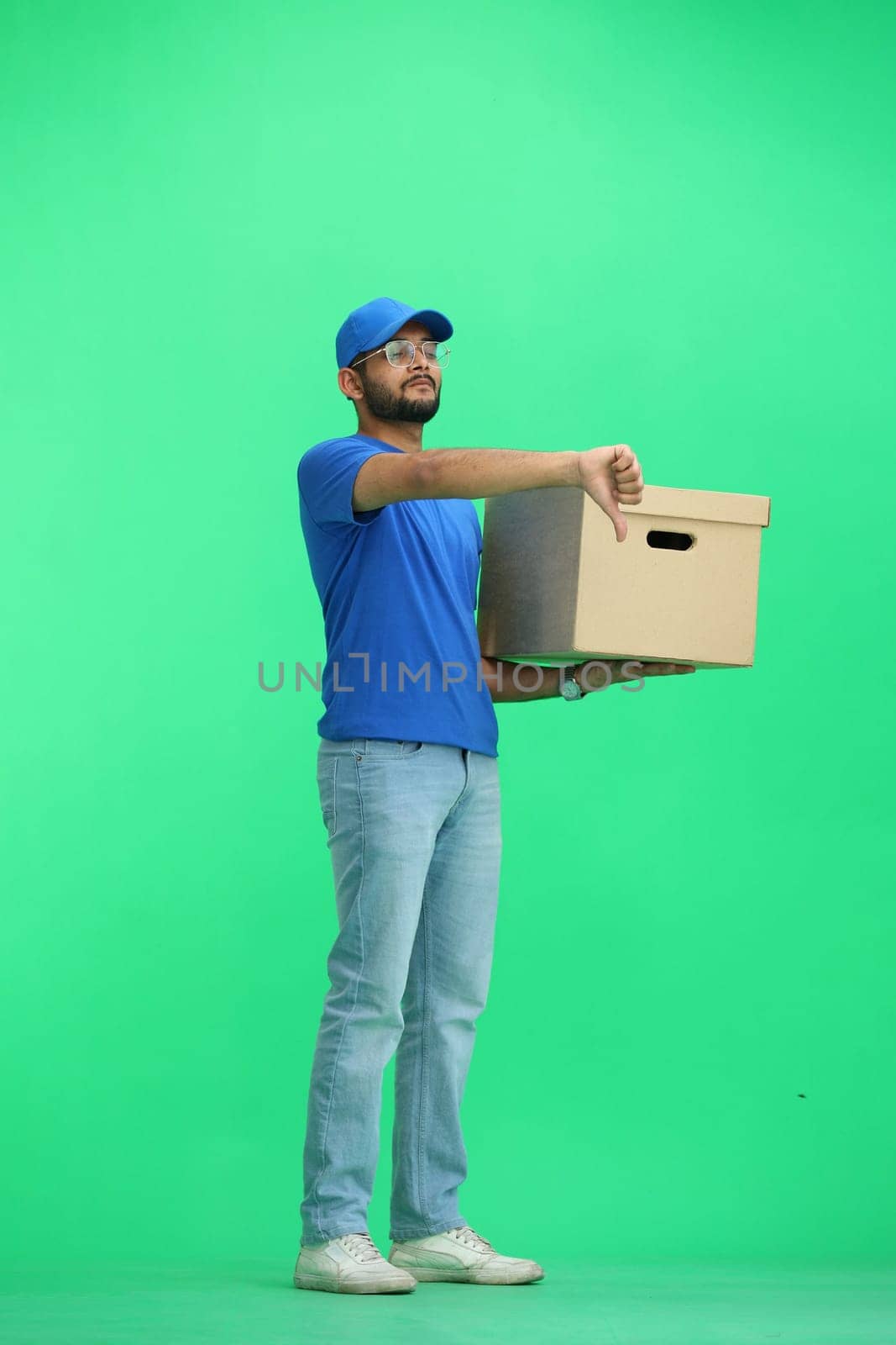 A male deliveryman, on a green background, full-length, with a box, shows his finger down.