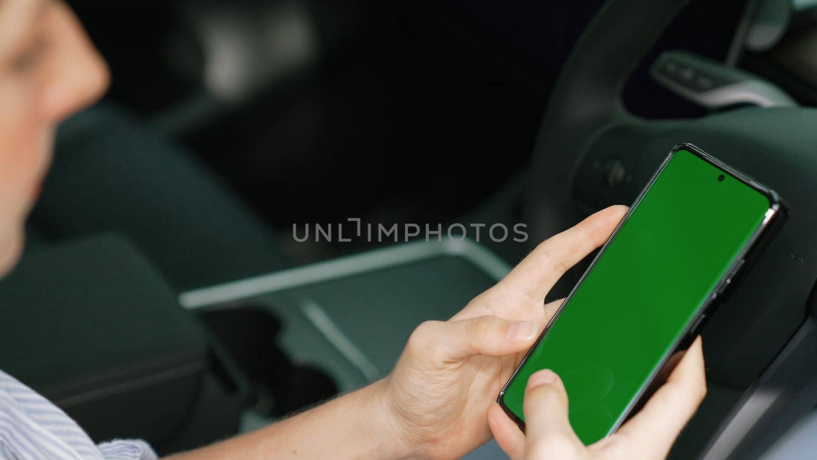 Holiday vacation road trip with environmental-friendly car concept. Eco-conscious woman on driver seat holding blank copyspace green screen smartphone for EV battery status. Exalt