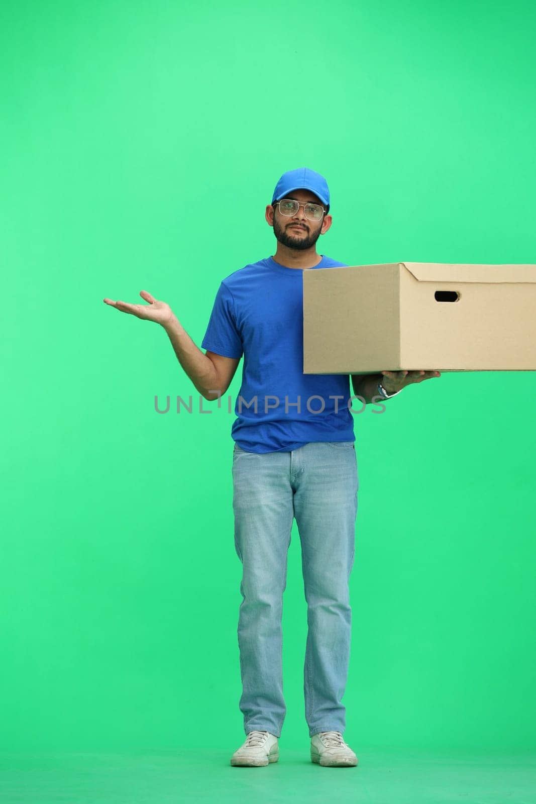 A male deliveryman, on a green background, full-length, with a box, points to the side by Prosto