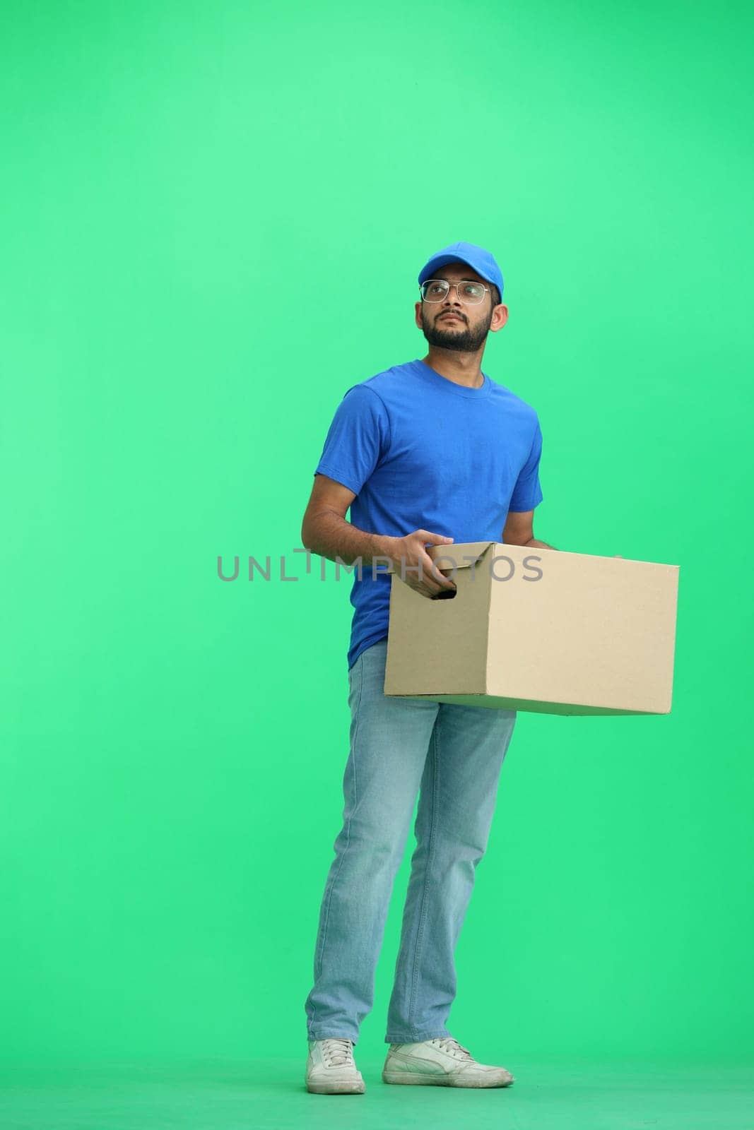 A male deliveryman, on a green background, full-length, with a box.