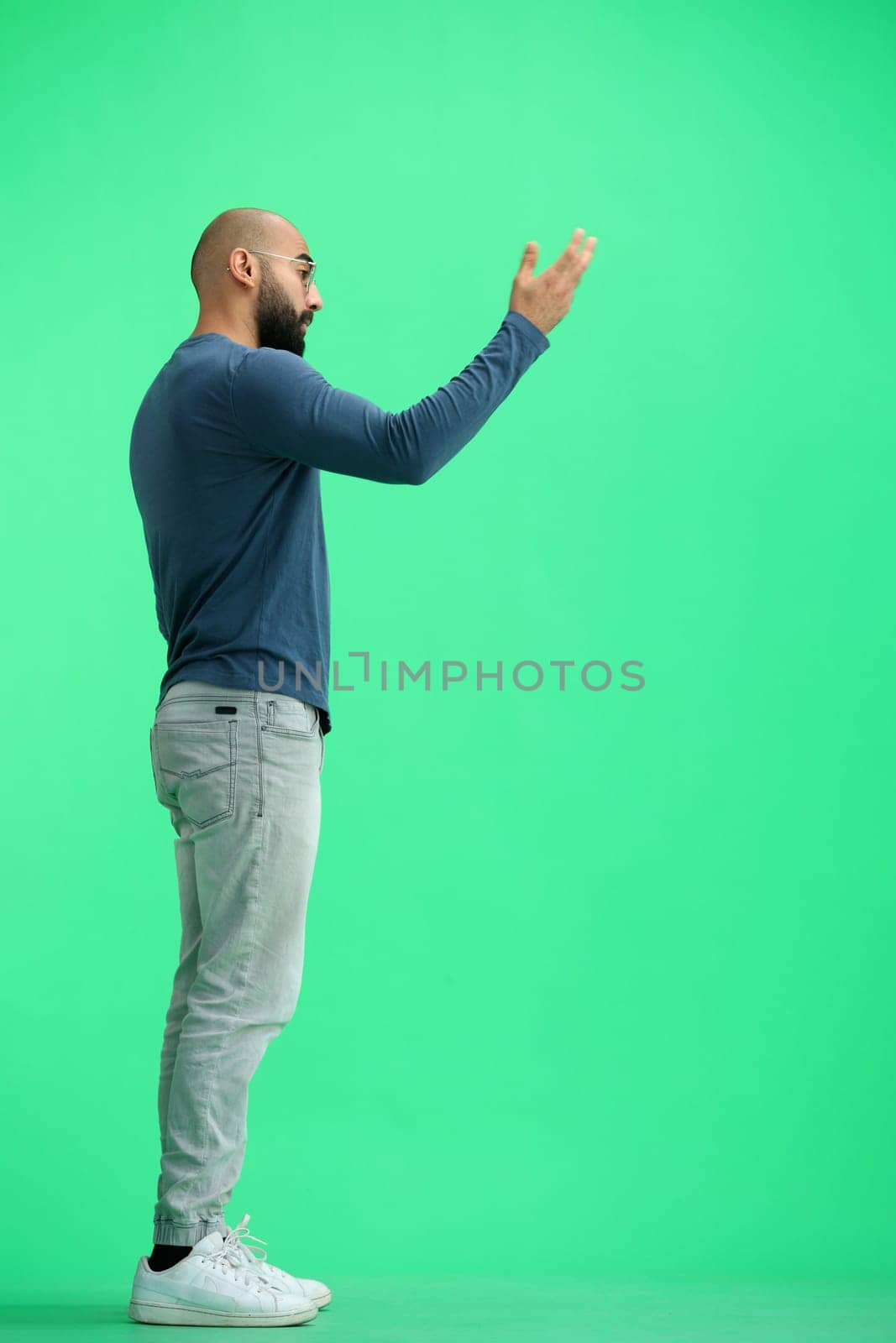 A man, on a green background, in full height, calls to himself.