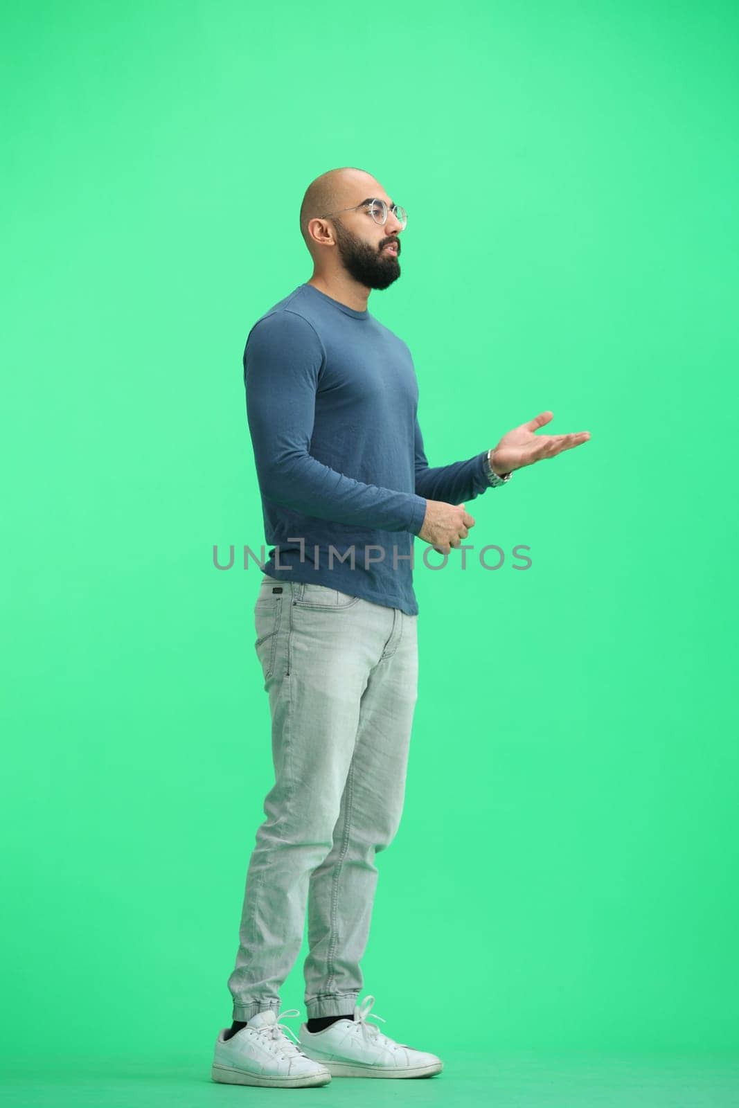 A man, on a green background, in full height, gestures.