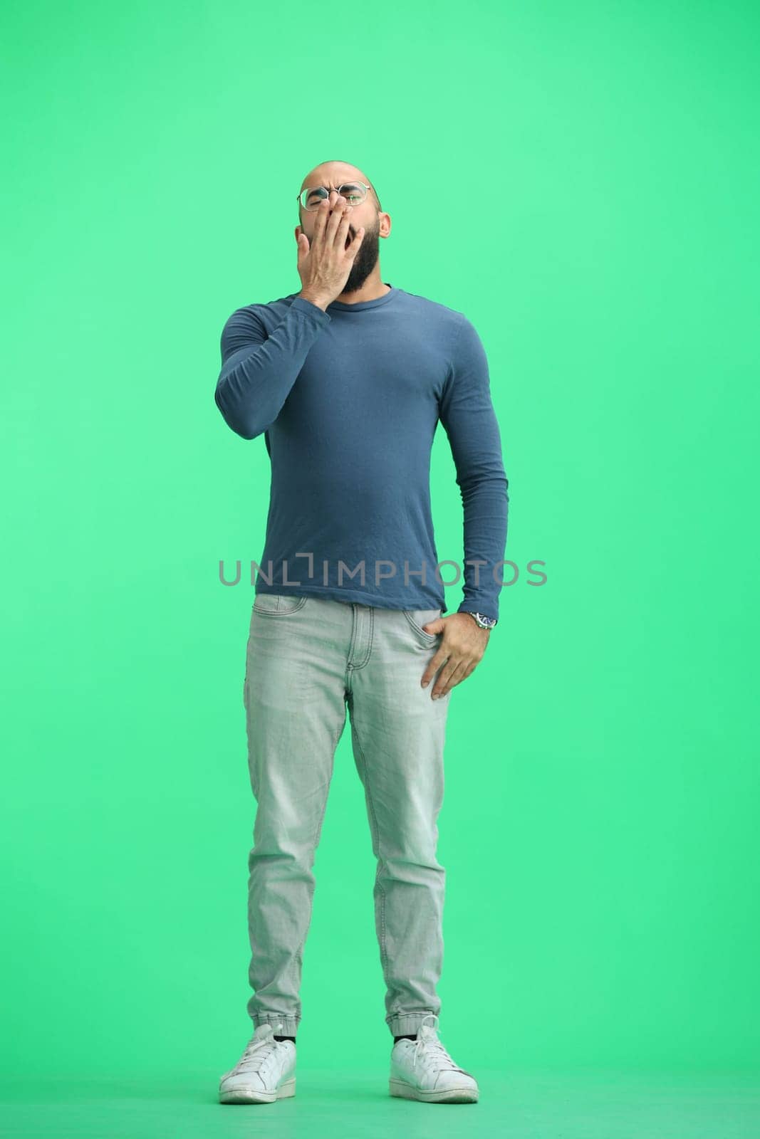 A man, on a green background, in full height, yawns.