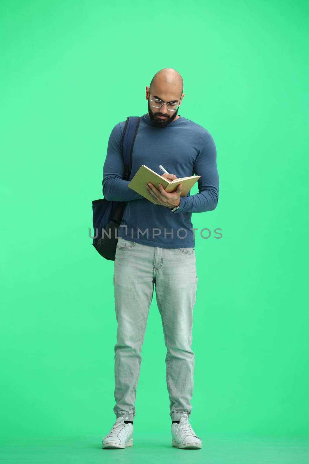 A man, on a green background, in full height, writes.