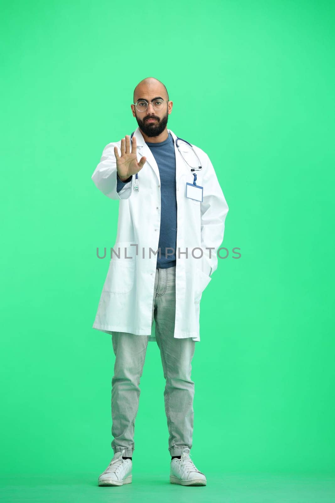 A male doctor, on a green background, in full height, shows a stop sign.